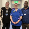 Three NHS staff from Yeovil spinal clinic stand in a row, with a skeleton model to their left, in what appears to be a ward at a hospital